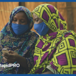 Two Liberian women using a mobile phone with masks, illustrating RapidPro Liberia’s role in connecting health workers through mHero.